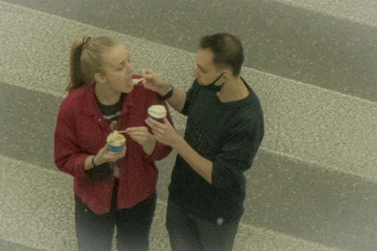 Man feeding a woman from a paper cup as they walk across a zebra crossing